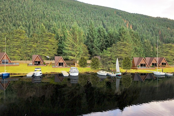 Timber holiday lodges on lake shore with sailing boats and jetty